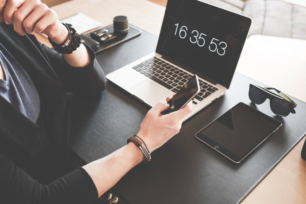 Woman Using a Smartphone While Fronting a Macbook Pro and Black Ipad